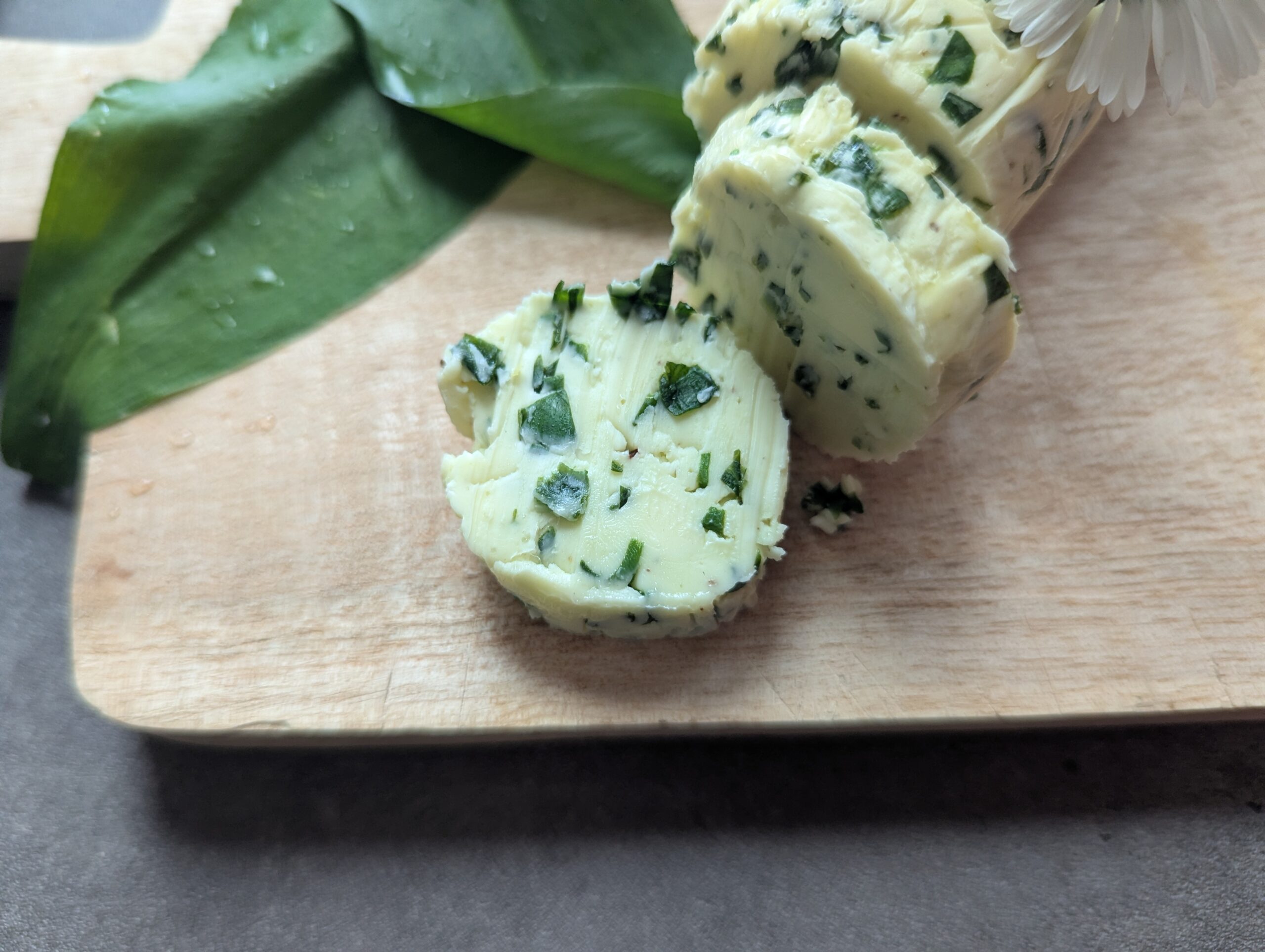 Bärlauchbutter in Scheiben auf einem rustikalen Holzbrett
